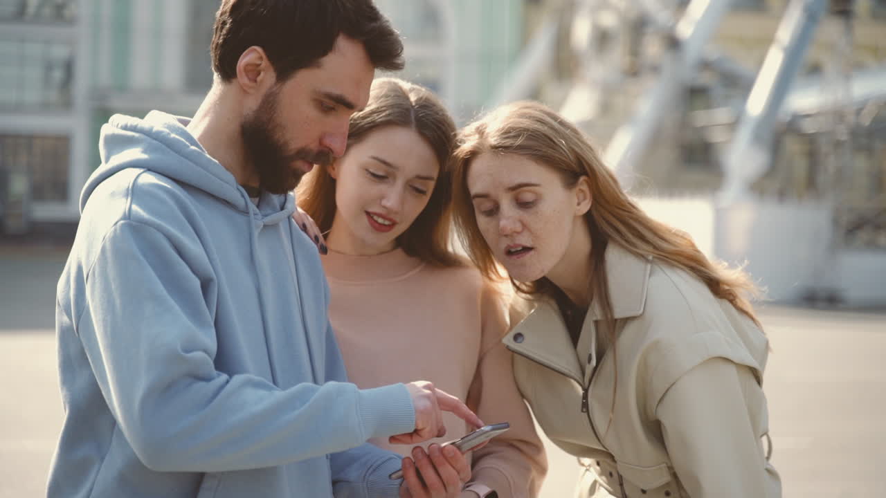 A Group Of Three Young Tourists In The City Search For An Address On The Cell Phone
