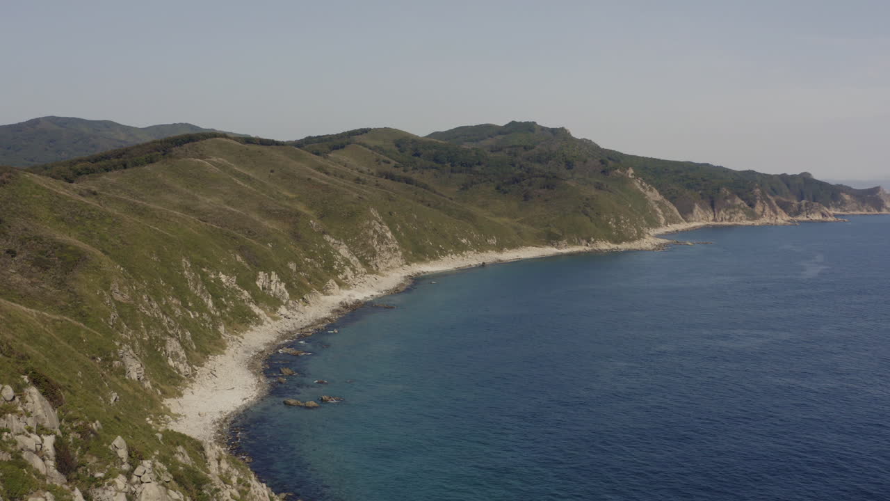 Sorvolo di un litorale roccioso a picco con oceano blu intenso in una giornata limpida e soleggiata.