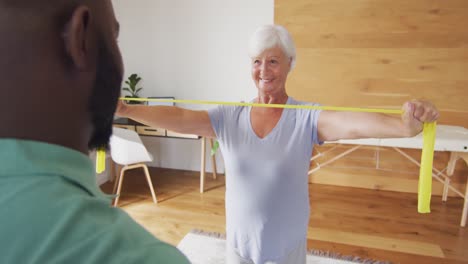 Video-Einer-Glücklichen-Kaukasischen-Seniorin,-Die-Mit-Einem-Afroamerikanischen-Physiotherapeuten-Trainiert