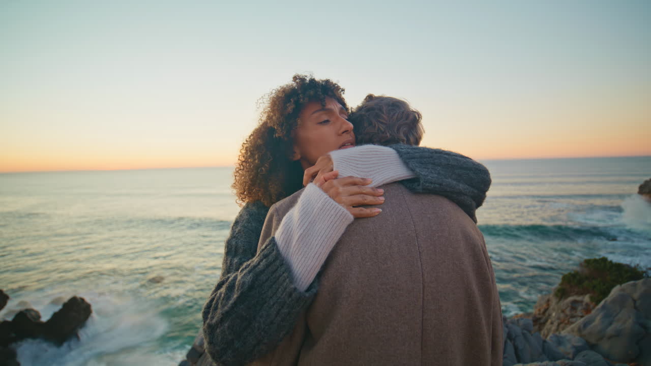 Peaceful lovers bonding sunset on seacoast closeup. Diverse spouses embracing