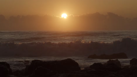 Toma-En-Cámara-Lenta-De-Naranja,-Sol-Dorado-Saliendo-Sobre-Nubes-Bajas-Y-Rompiendo-Olas