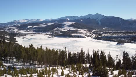 Flying-towards-frozen-lake-with-snow-covered-mountains-in-the-background,-aerial