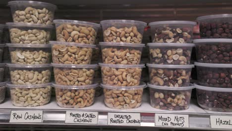 los cacahuetes mixtos y los bocadillos de anacardos se sientan en un estante de supermercado en recipientes de plástico