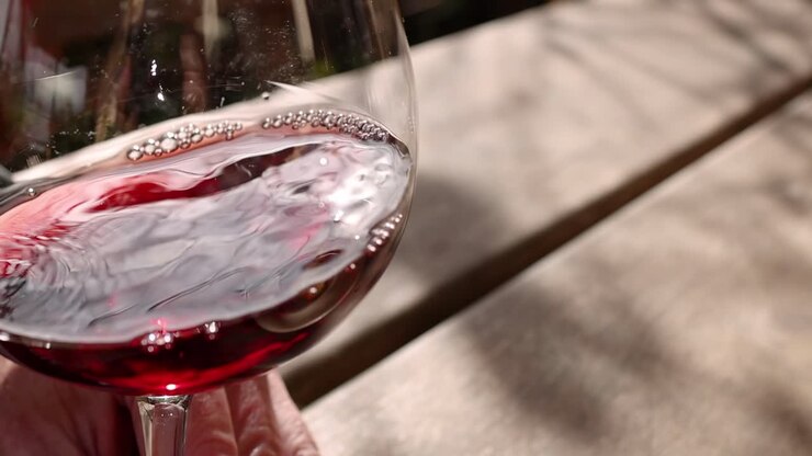 Eine detaillierte Ansicht von Rotwein, der in einem Glas wirbelt und Schatten auf eine Holzoberfläche wirft.