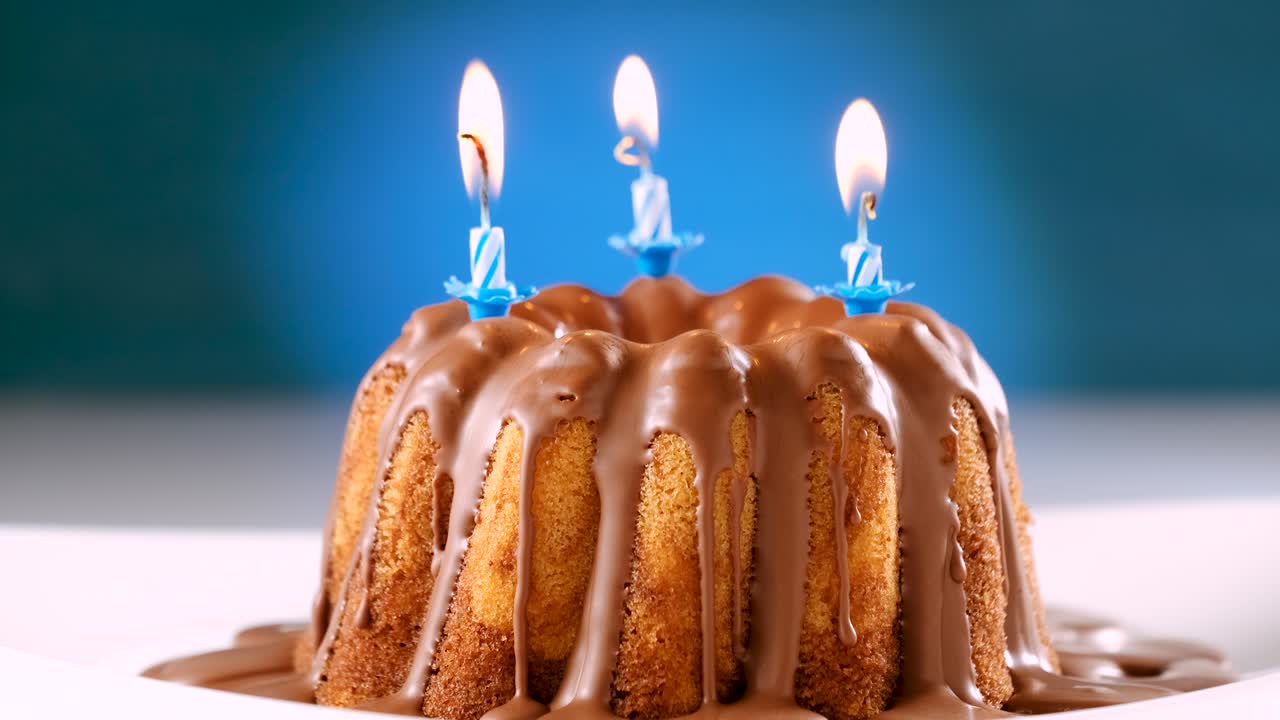 चॉकलेट नौगट आइसिंग वाले मार्बल केक पर जलती हुई नीली जन्मदिन की मोमबत्तियाँ