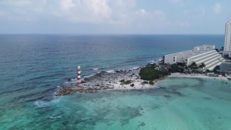 Vista-Aérea-De-Drones-Alejándose-Del-Faro-De-Punta-Cancún,-Un-Hito-En-Cancún,-México,-Rodeado-Por-Aguas-Turquesas-Del-Mar-Caribe