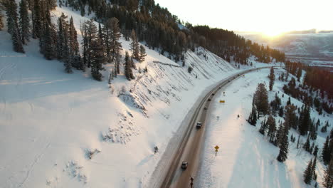 Vista-Aérea-Del-Tráfico-Por-Carretera-En-El-Paisaje-Montañoso-Nevado-Al-Atardecer