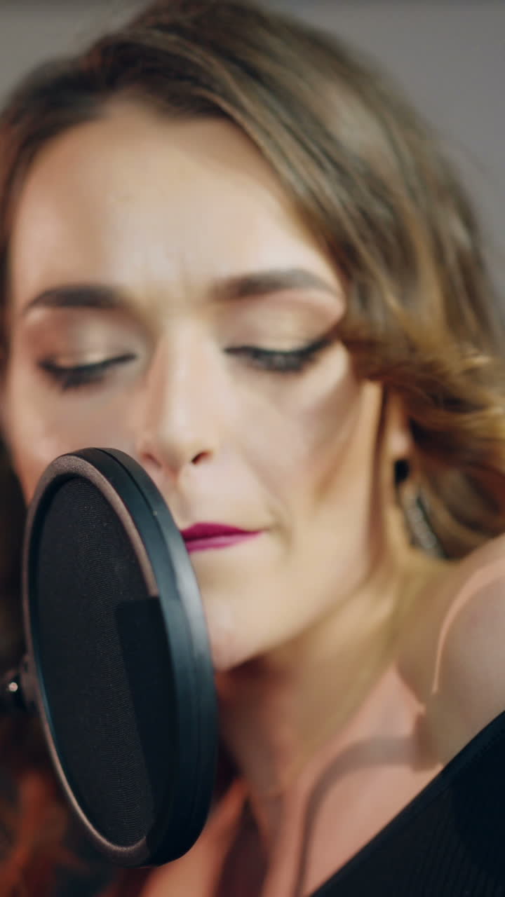 beautiful singer with curly hair is singing a song in an audio recording studio on the background of professional equipment. Close-up Vertical video