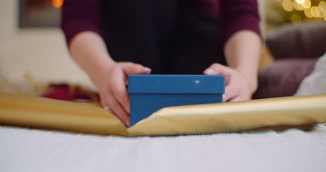 woman wrapping christmas present with golden gift paper