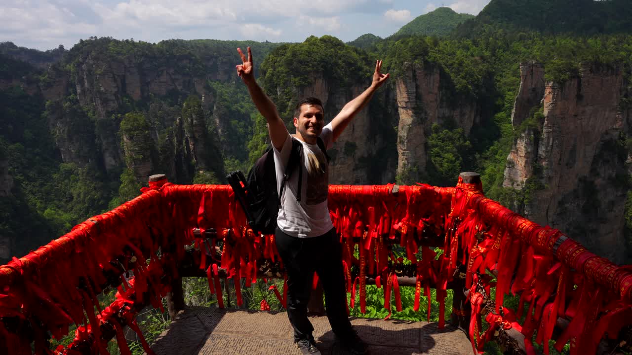 Excited photographer extends his arms in a V sign while admiring the landscape of Yuanjiajie, China