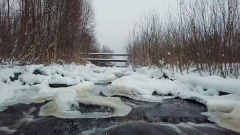 low altitude drone flight over iced and snowy water stream