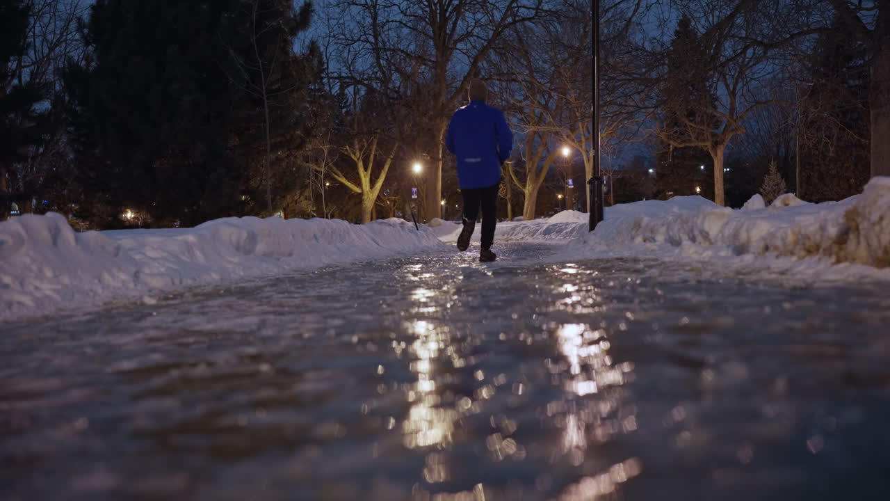 Person over 50 jogging cautiously on a frozen snow-lined path at night, using crampons for safety, embracing movement, and well-being in a beautiful outdoor winter setting in Montreal, Canada.