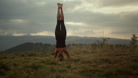 chica de pie sobre la cabeza en un paisaje montañoso. entrenador practicando yoga en el suelo