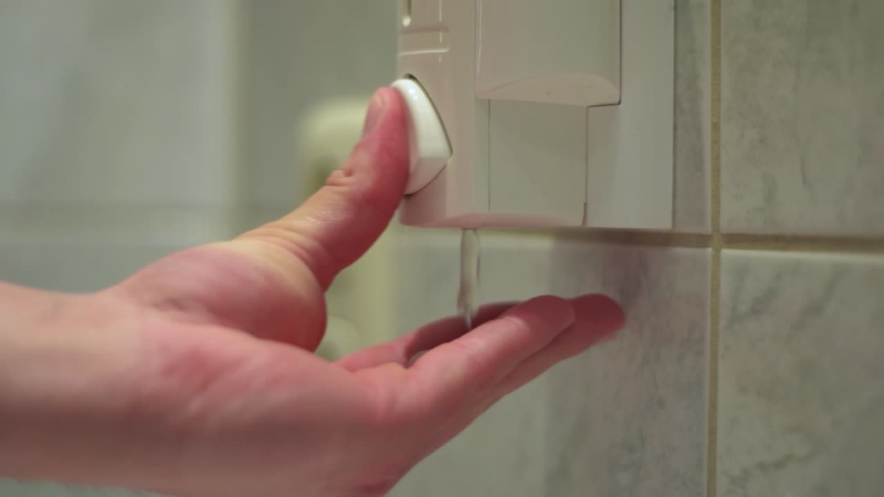 primer plano de la mano masculina recibiendo una dosis de jabón líquido de un dispensador de jabón en el baño