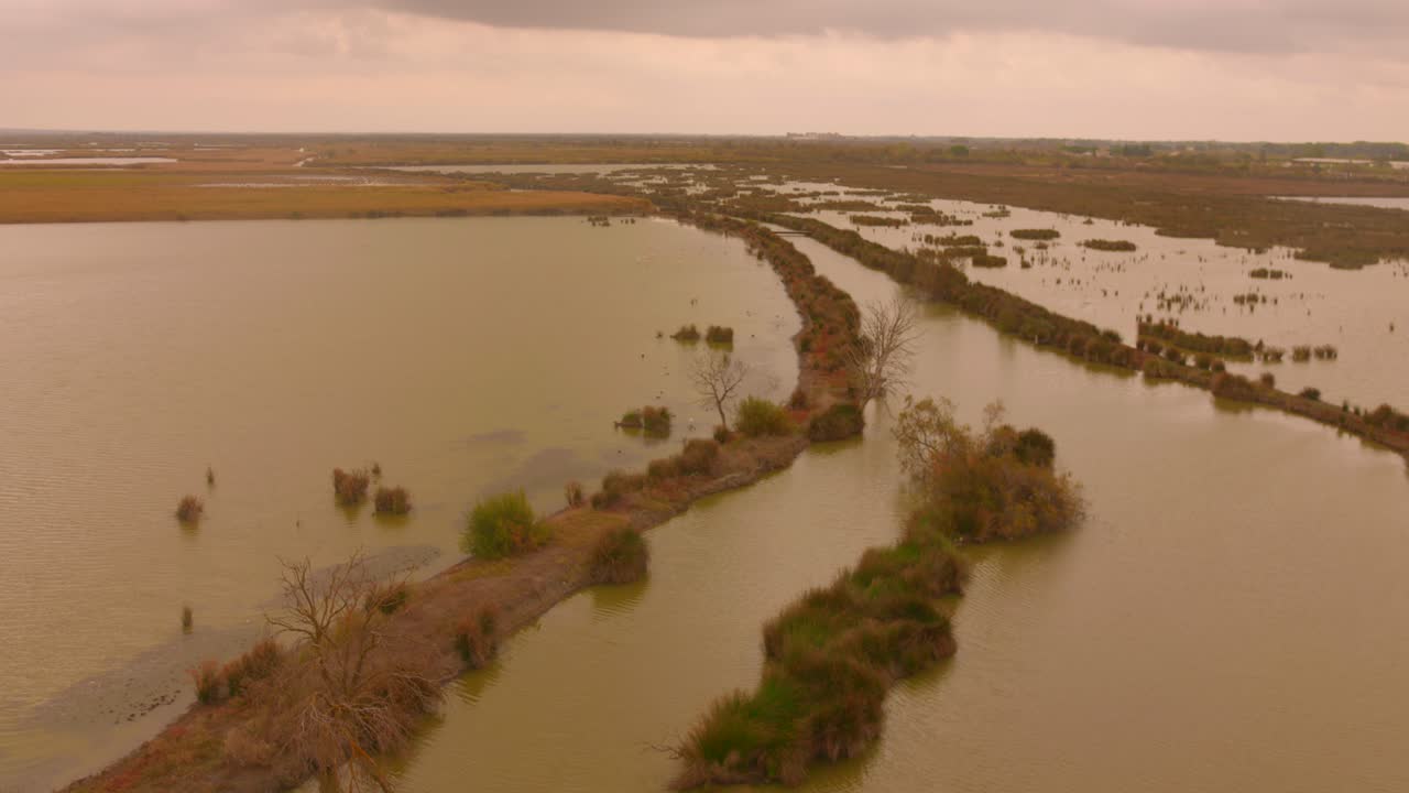 Palude tranquilla al crepuscolo vicino ad Aigues-Mortes, Francia, con strette strisce di terra attraverso acqua marrone in una giornata nuvolosa. Ampia ripresa aerea