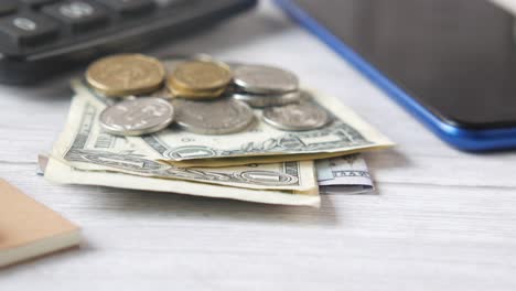 dinero, monedas, calculadora, teléfono, cuaderno y bolígrafo en una mesa blanca de madera