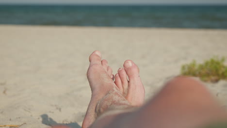 escena de playa relajante con pies de hombre de arena en primer plano y olas en el fondo