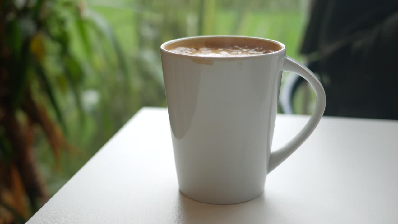 Hand reaching for a coffee mug on a white table in a cafe setting