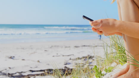 sección media de una mujer usando un teléfono móvil en la playa 4k