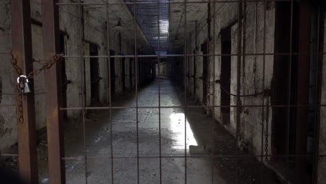 decrepit prison cellblock seen through padlocked gate