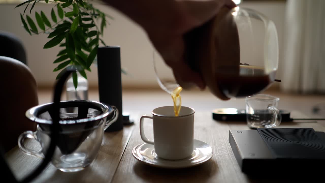 Dolly view of a hand pouring hot fresh specialty coffee with a glass kettle in a white cup during breakfast