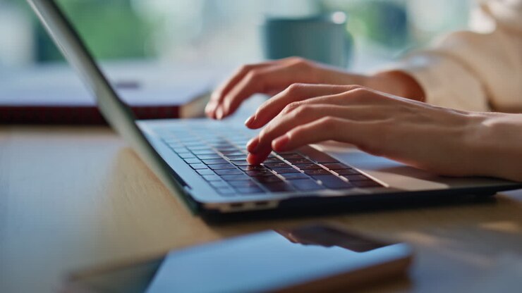 Nahaufnahme von zarten Fingern, die auf einem Laptop in einer Büroumgebung tippen. Lächelnde Geschäftsfrau