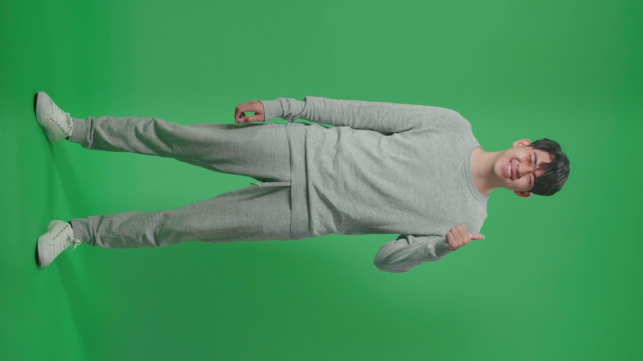 Full Body Of Asian Man Showing Thumbs Up Gesture And Smiling While Standing In The Green Screen Studio