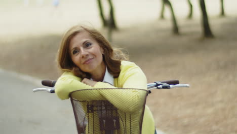 Smiling-woman-leaning-against-handlebars-of-bike