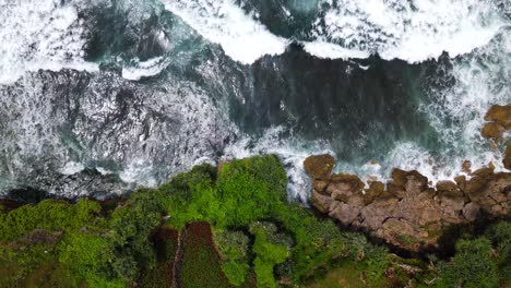 aerial overhead shot of powerful waves of sea crashing against rocky coastline