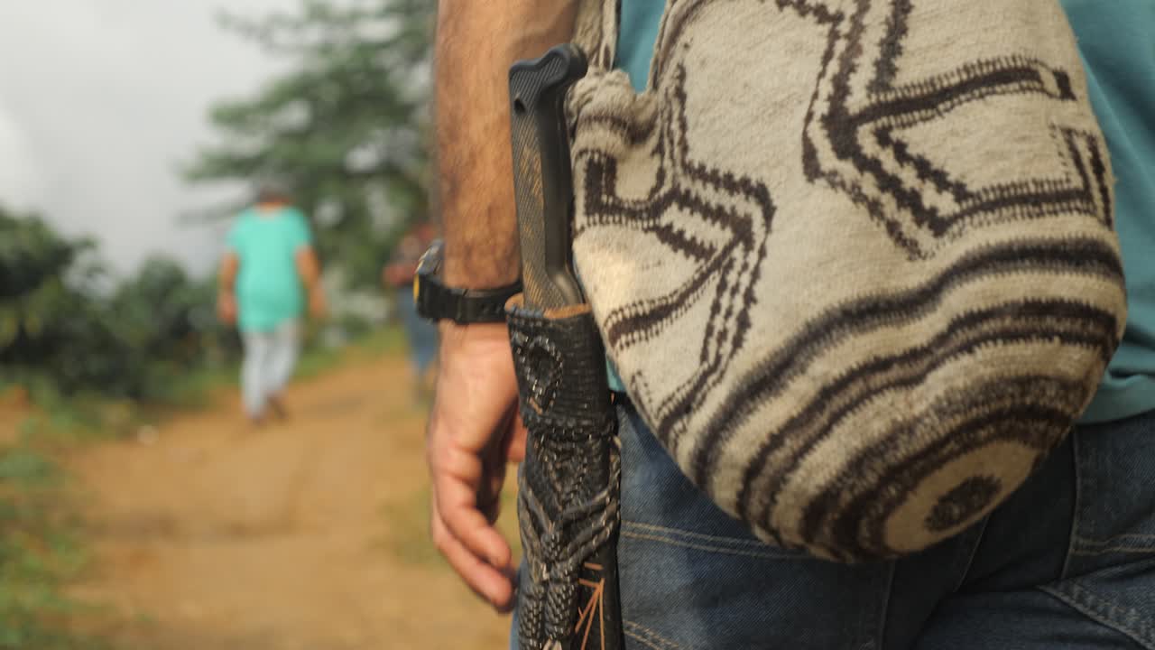 A coffee farmer walks with bag and knife on dirt road to the plantation to harvest the beans in forest jungle seeing only the middle body of Sierra Nevada Colombia