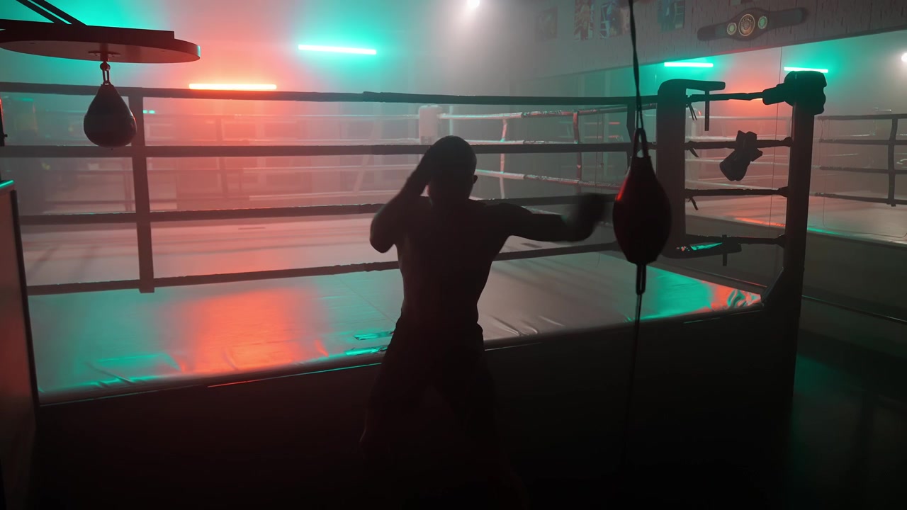 Silhouette eines Boxers beim Training am Speed Bag in dunklem Fitnessstudio
