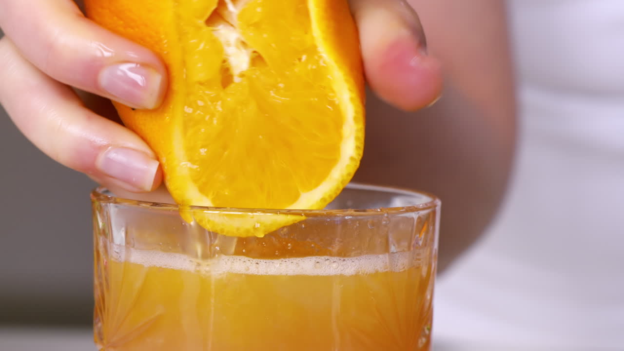 Una mujer exprime el zumo de una naranja en un vaso a cámara lenta.