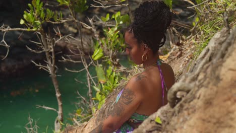 atop a cliff, a young woman in a flowing gown gazes down at the sandy shore