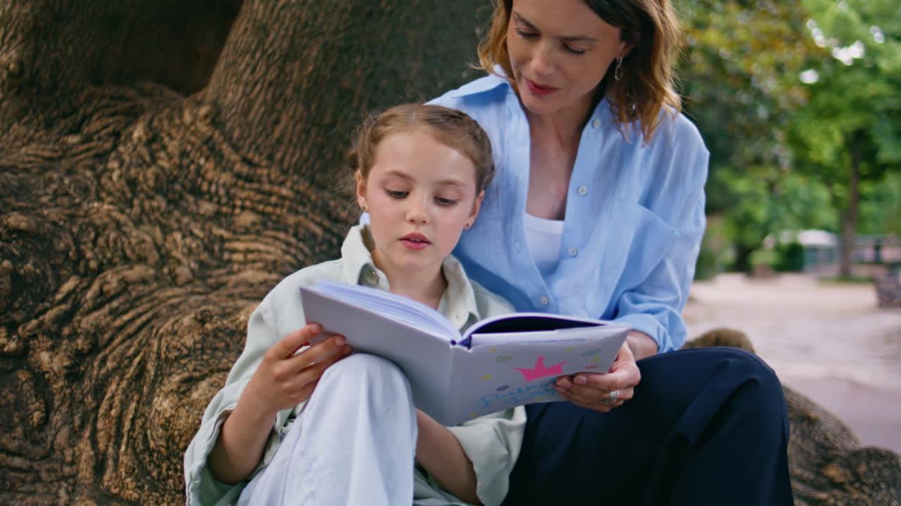 Cute family reading novel resting together at big roots tree at greenery park