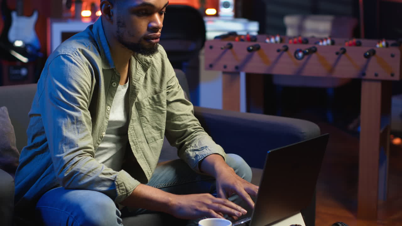 Vertical Video Focused African American guy teleworking on his laptop in a stylish living room