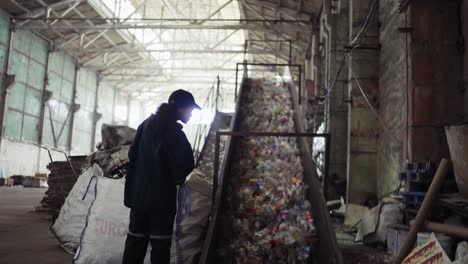 A-young-African-American-woman-checks-a-conveyor-belt-at-a-recycling-plant.-Pollution-control.-Zoom-in