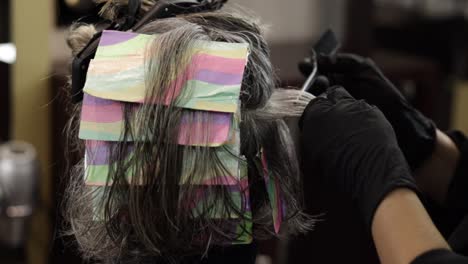 woman with grey hair undergoing a salon transformation as she receives a hair color treatment with foils