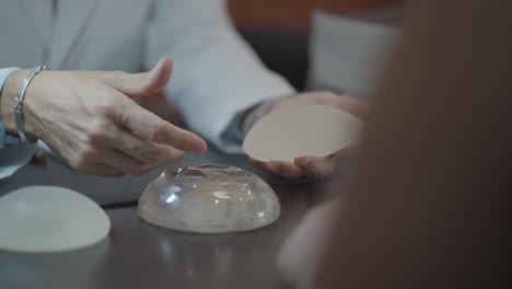 el médico muestra a la paciente una prótesis de mama de silicona