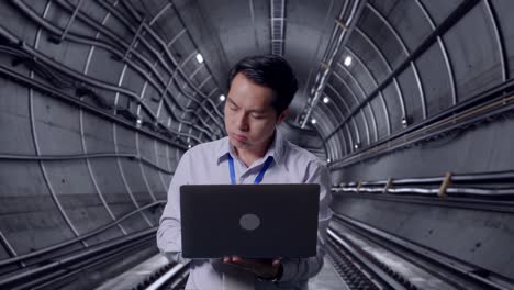 asian male professional worker standing with his laptop in underground subway tunnel, he is nodding his head with dissapionted