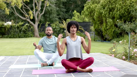 focused african american couple practicing yoga meditation sitting in garden, slow motion