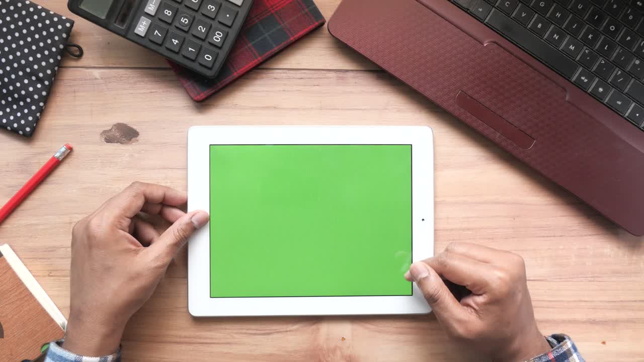 Person using tablet with green screen on a wooden desk