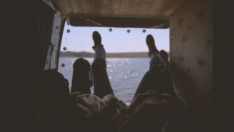 two girls are lying in the back of a caravan by a lake