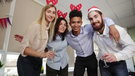 gente de negocios feliz con sombreros de santa se está haciendo selfie mirando a la cámara y sonriendo mientras celebra el año nuevo en la oficina