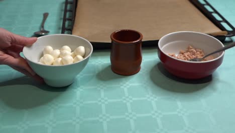 woman leaving bowl with mozzarella balls on turquoise table, ingredients for pizza