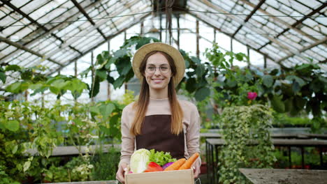 woman holding a crate of fresh vegetables in a greenhouse
