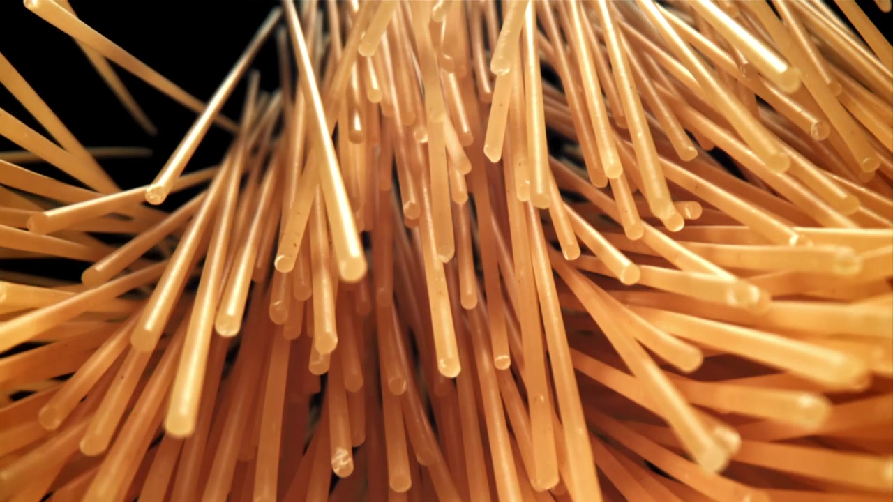 Primo piano di spaghetti crudi che si sollevano su sfondo nero