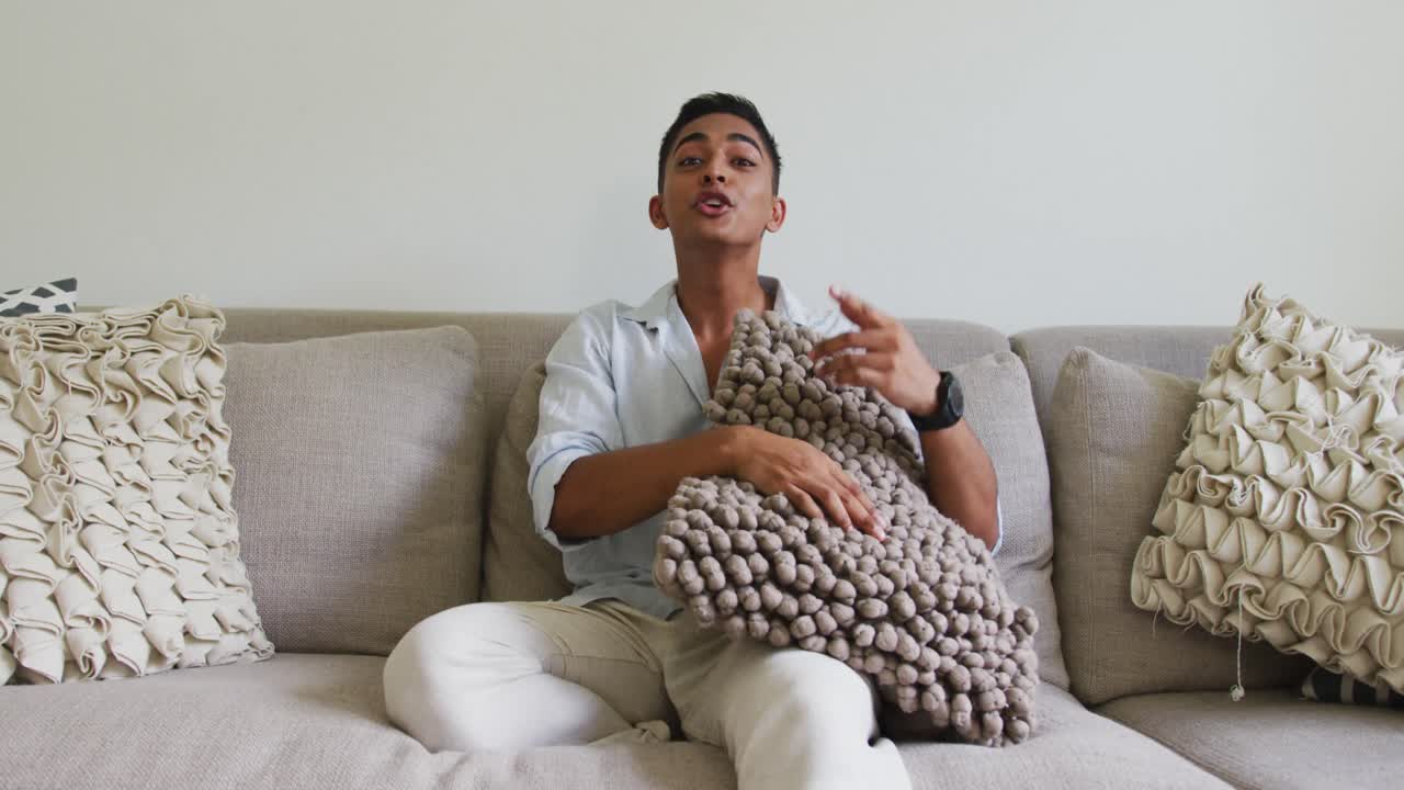 소파 에 앉아 베개 를 들고 이야기 하는 미소 짓는 혼합 인종 남자