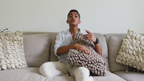 smiling mixed race man sitting on sofa holding cushion and talking