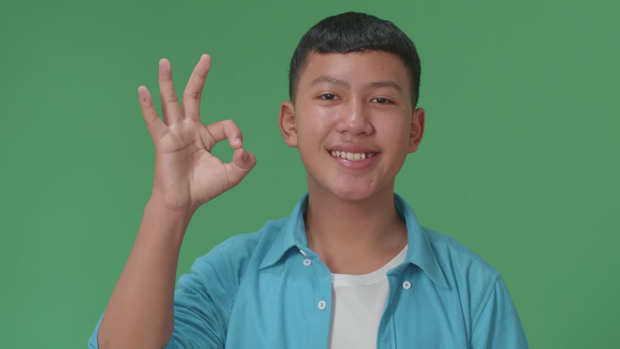 A Portrait Of A Happy Young Asian Boy Showing Okay Gesture To The Camera In The Green Screen Studio