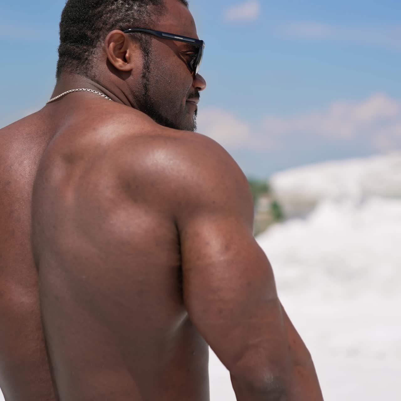 Dark skinned bodybuilder in black glasses. Back muscles of african american sportsman. Shirtless black athlete posing outdoors in summer
